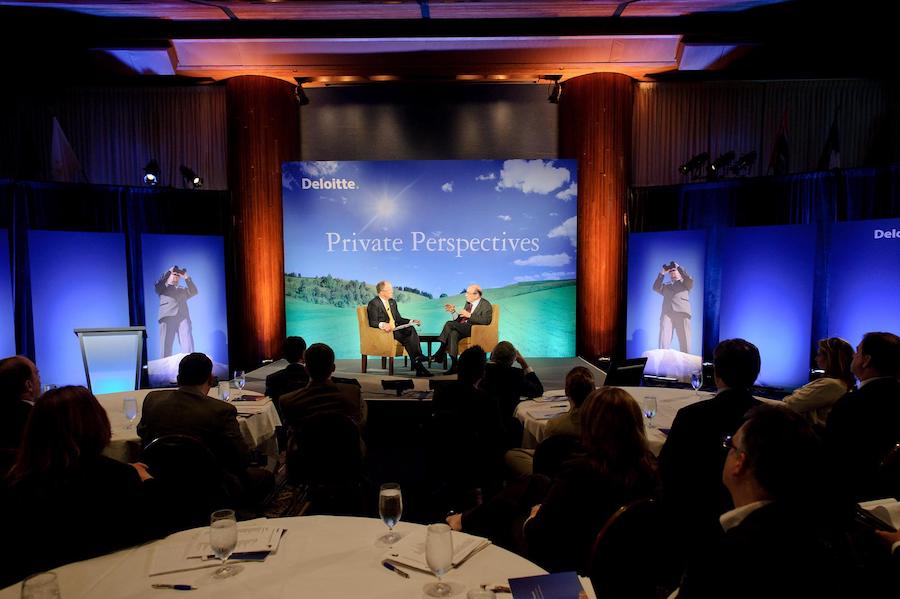 A professional conference session titled "Private Perspectives" with two speakers engaged in discussion on stage, surrounded by an attentive audience in a dimly lit venue.