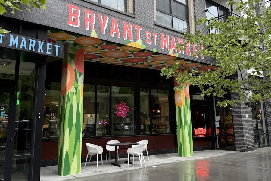 A vibrant, flower-painted entrance of Bryant Street Market with two white chairs and a table outside on a rainy day.