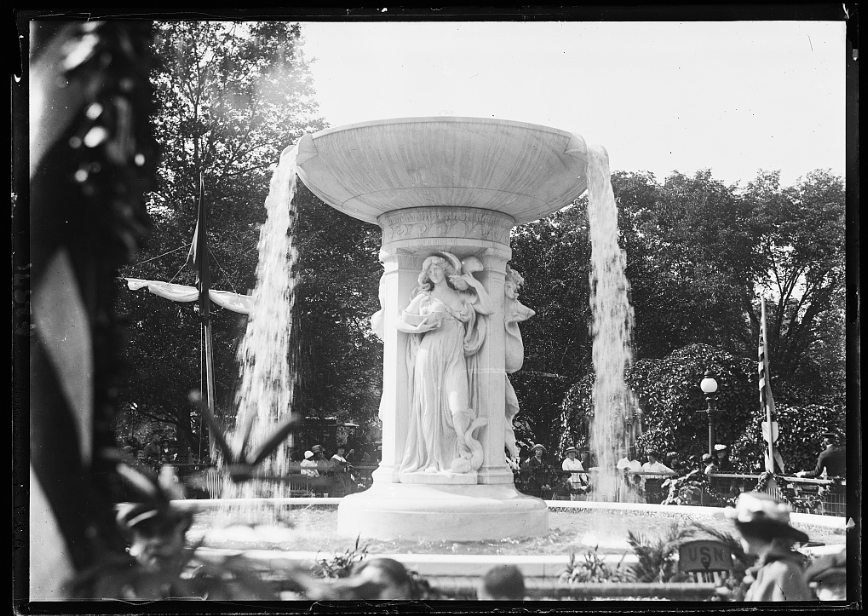 Historic photo of the Dupont Circle Fountain with sculpted figures and cascading water, surrounded by trees and people.