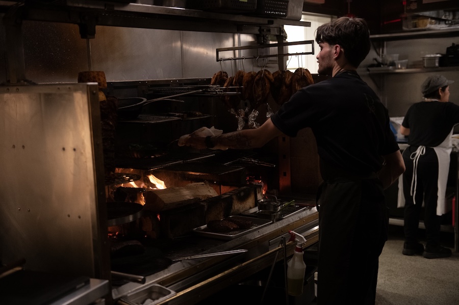 A chef tends to a wood-fired grill in a busy open kitchen in Washington, DC