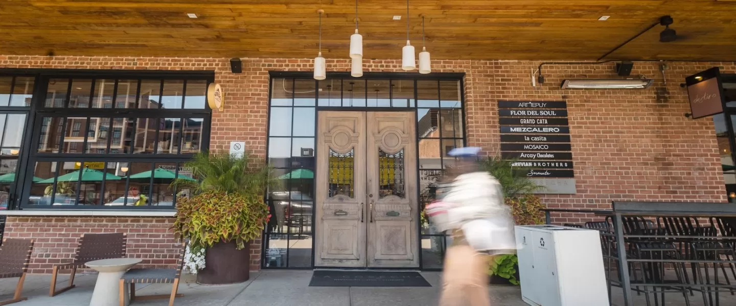 The exterior of La Cosecha, with an ornate wooden door, plants, hanging lights, and furniture outside. 