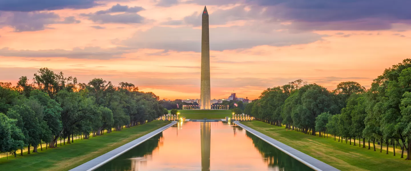 The Washington Monument glows at sunset with a colorful sky reflected in the Lincoln Memorial Reflecting Pool in Washington, DC.