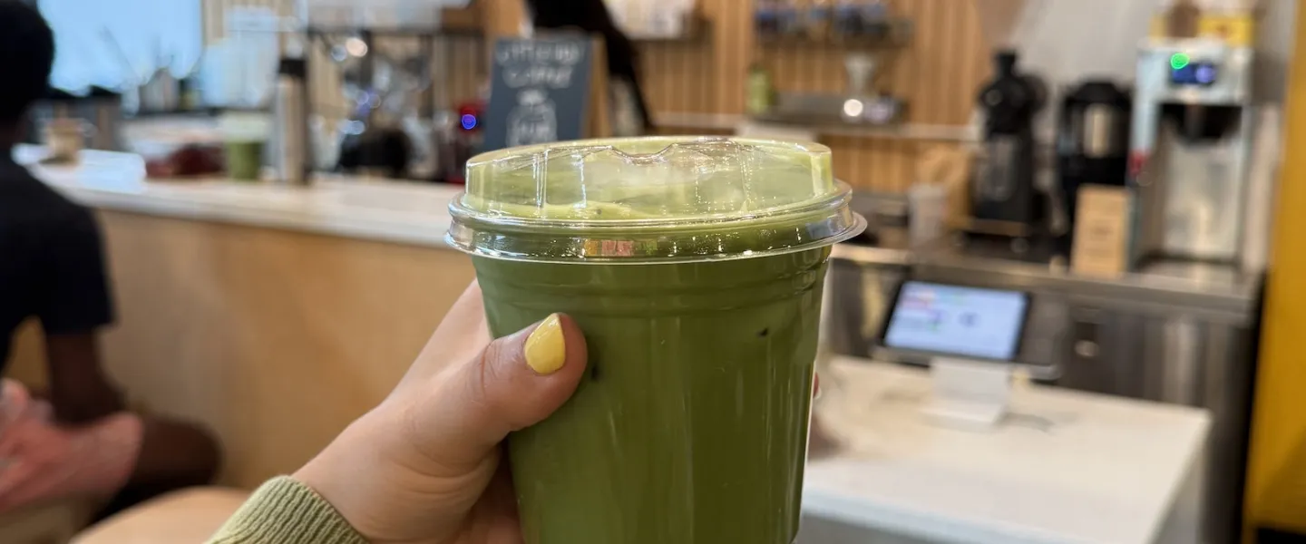 A hand holds up a matcha drink.