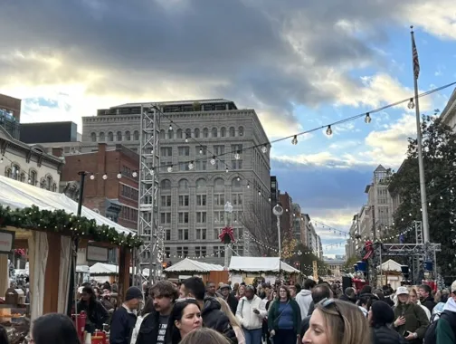 Holiday market scene in Downtown DC with crowds, festive decorations, and string lights.