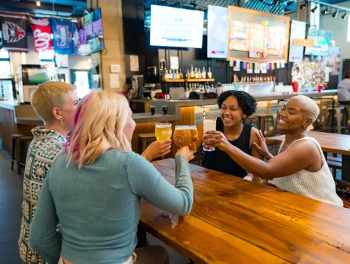 Two couples smile and clink their beers together at a brewery. 