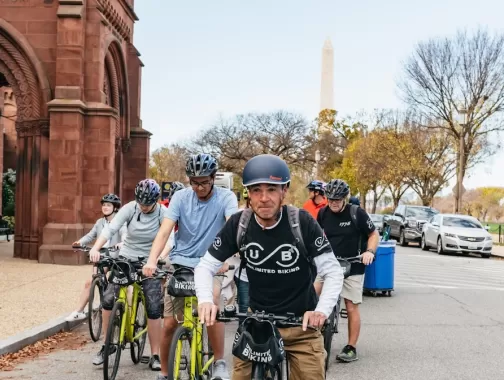 A guide leads a biking tour along the National Mall with the Smithsonian Castle and the Washington Monument in the background. 