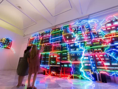 Two people look at a large, neon art installation that replicates the U.S.