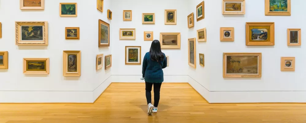  A visitor explores a gallery at The Phillips Collection, where small framed paintings in various styles are arranged on white walls, creating an immersive art experience.