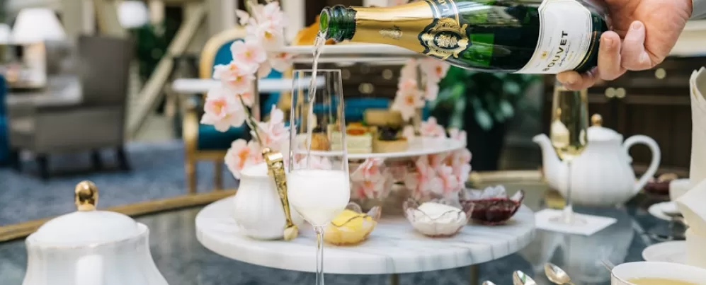 A hand pours champagne into a glass on a table set for a lavish high tea. 