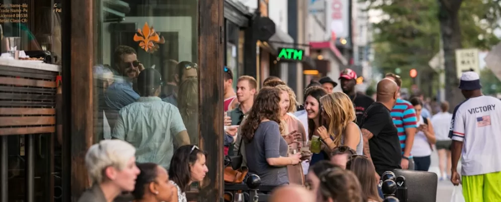 A lively crowd gathers outside Pearl Dive Oyster Palace, mingling and enjoying drinks along a bustling 14th Street sidewalk.