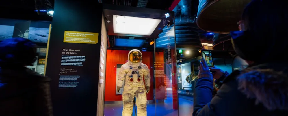 A visitor takes a photo of Neil Armstrong’s Apollo 11 spacesuit on display behind glass.
