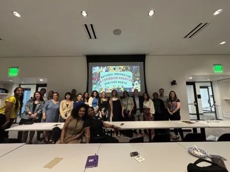 A group poses in front of a presentation screen during a National Immigration and Caribbean American Heritage Month snack and learn at Destination DC.